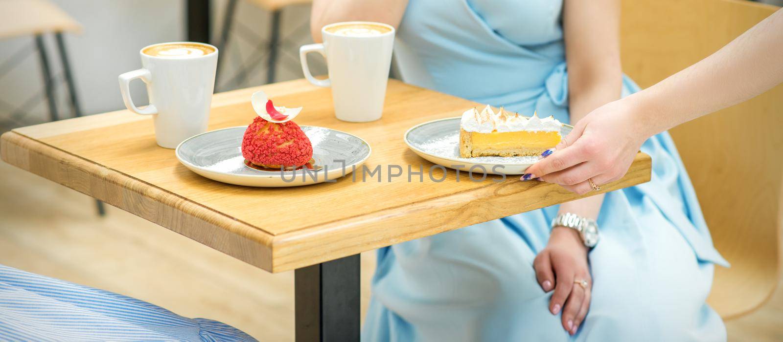 The waitress's hand puts the piece of cupcake on the table at a cafe, woman hand is putting round little pastry on the table on a background of a female in a blue dress