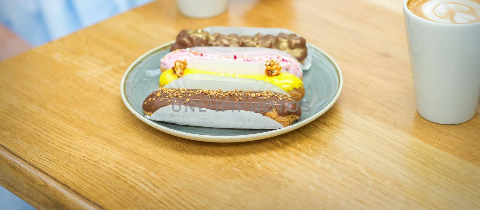 Several different eclairs on a plate are on the table with a cup of coffee in a cafe