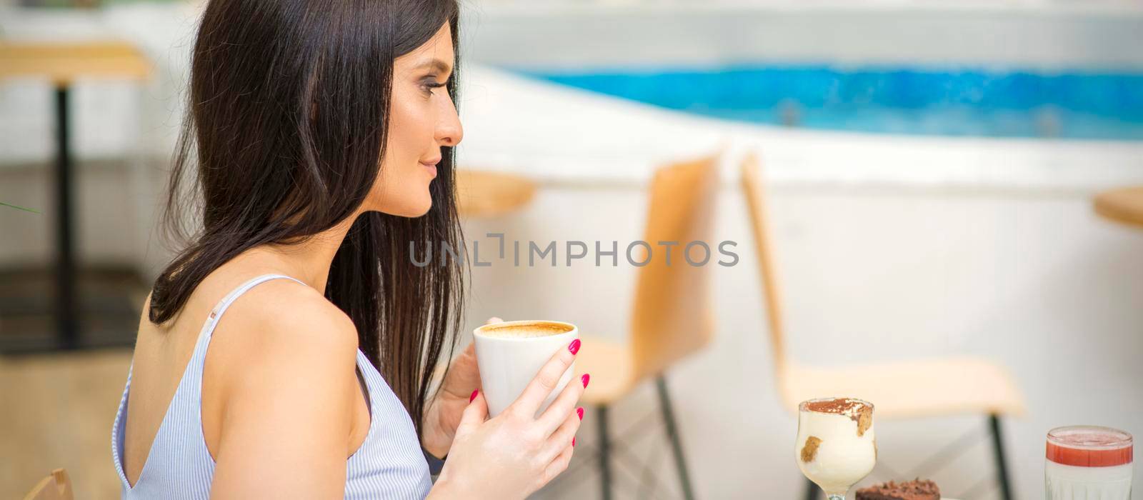 The side view of a young woman drinking coffee resting at the resort at a cafe outdoors. by okskukuruza