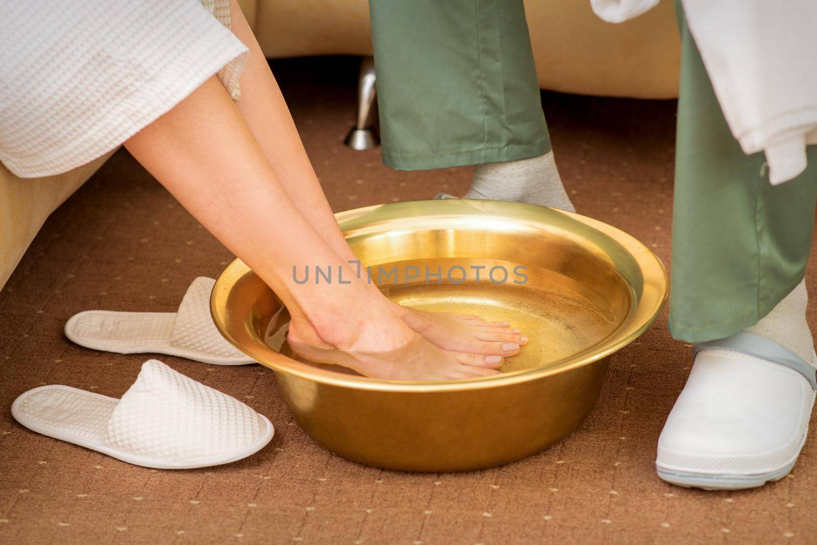Female feet in a golden bowl with water in spa salon. Spa treatment