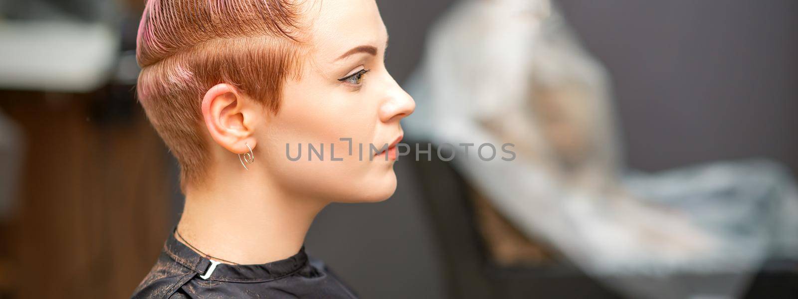 Side view portrait of a beautiful young caucasian woman with a short pink haircut waiting for a hairdresser in a beauty salon