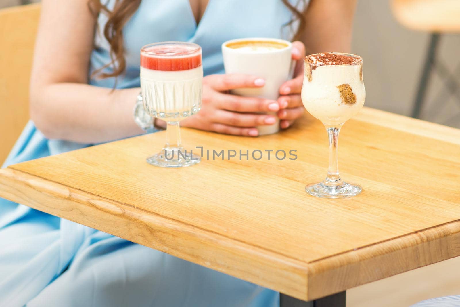 Hands of a young woman holding a cup of coffee with different cocktails on the table at the cafe