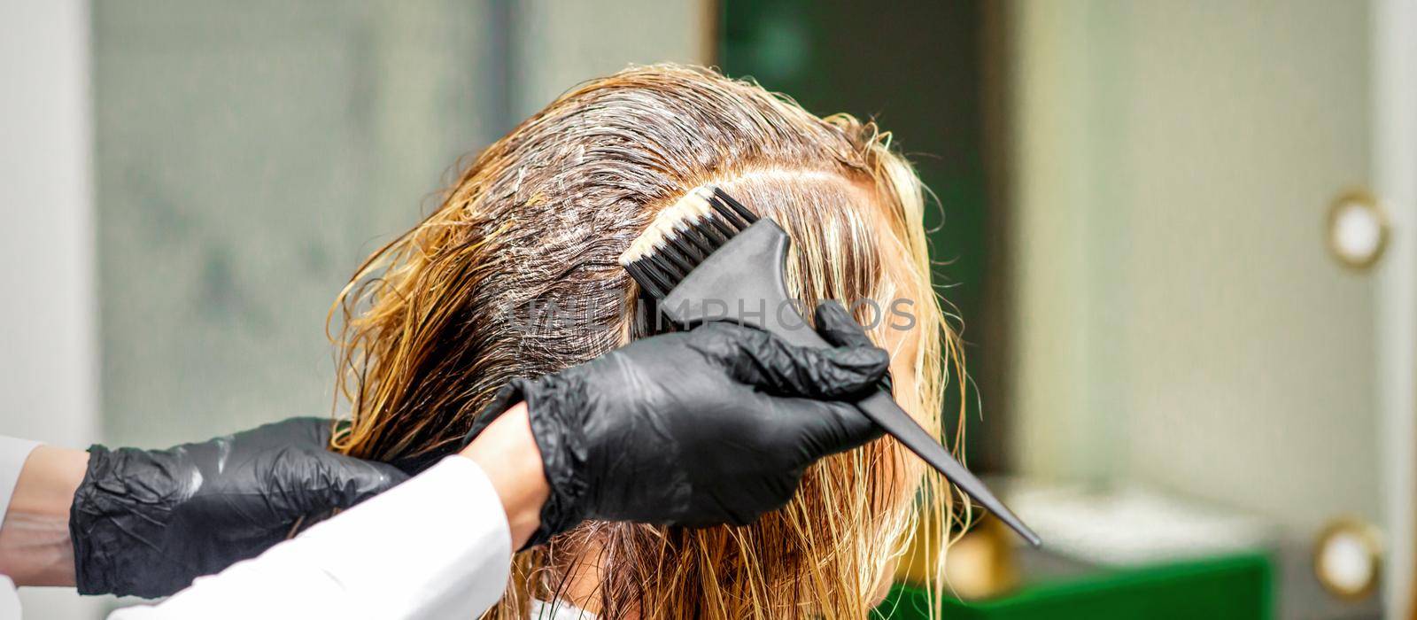 Hand of a hairdresser in black gloves applying dye to the female hair in a beauty salon