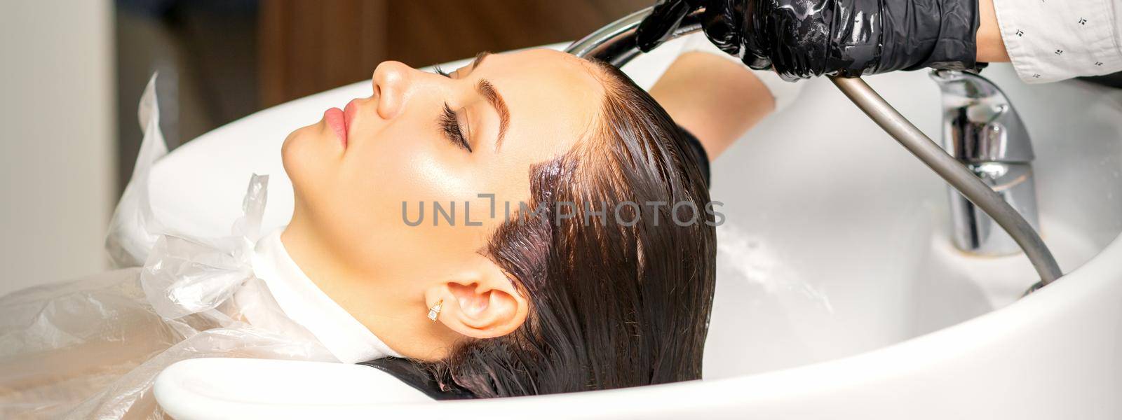Male hairdresser washing hair in the sink to the female client before making hairstyling in a beauty salon