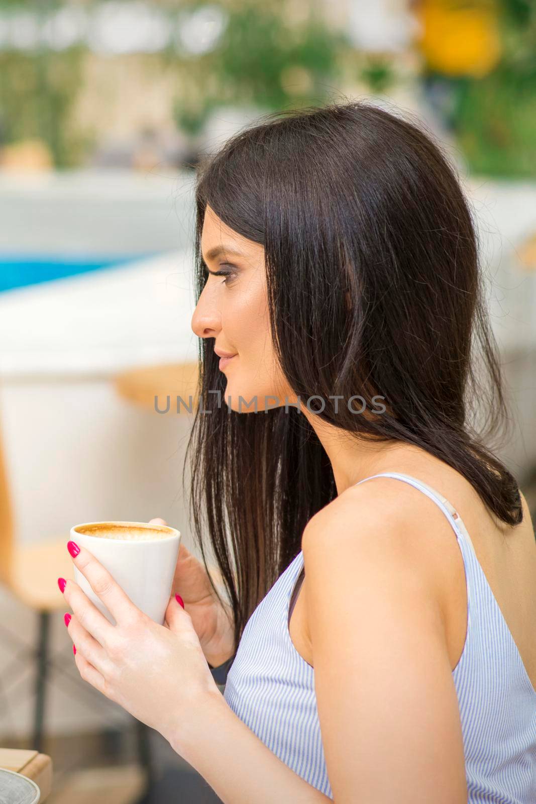 The side view of a young woman drinking coffee resting at the resort at a cafe outdoors