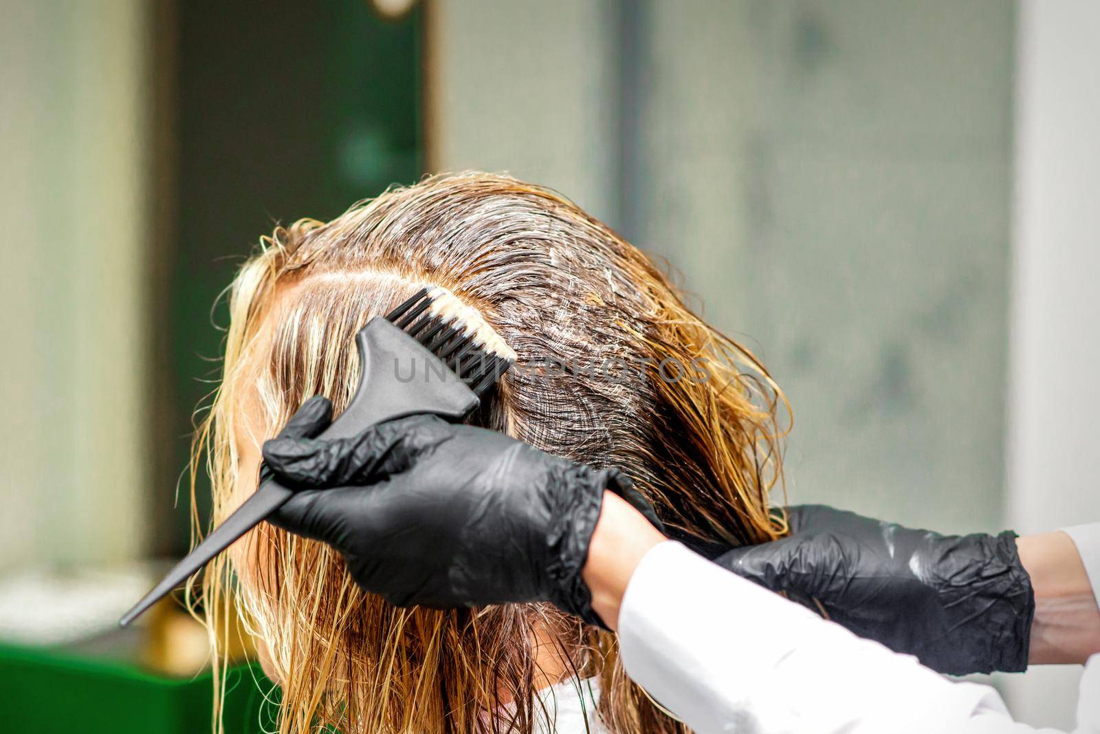 Hand of a hairdresser in black gloves applying dye to the female hair in a beauty salon