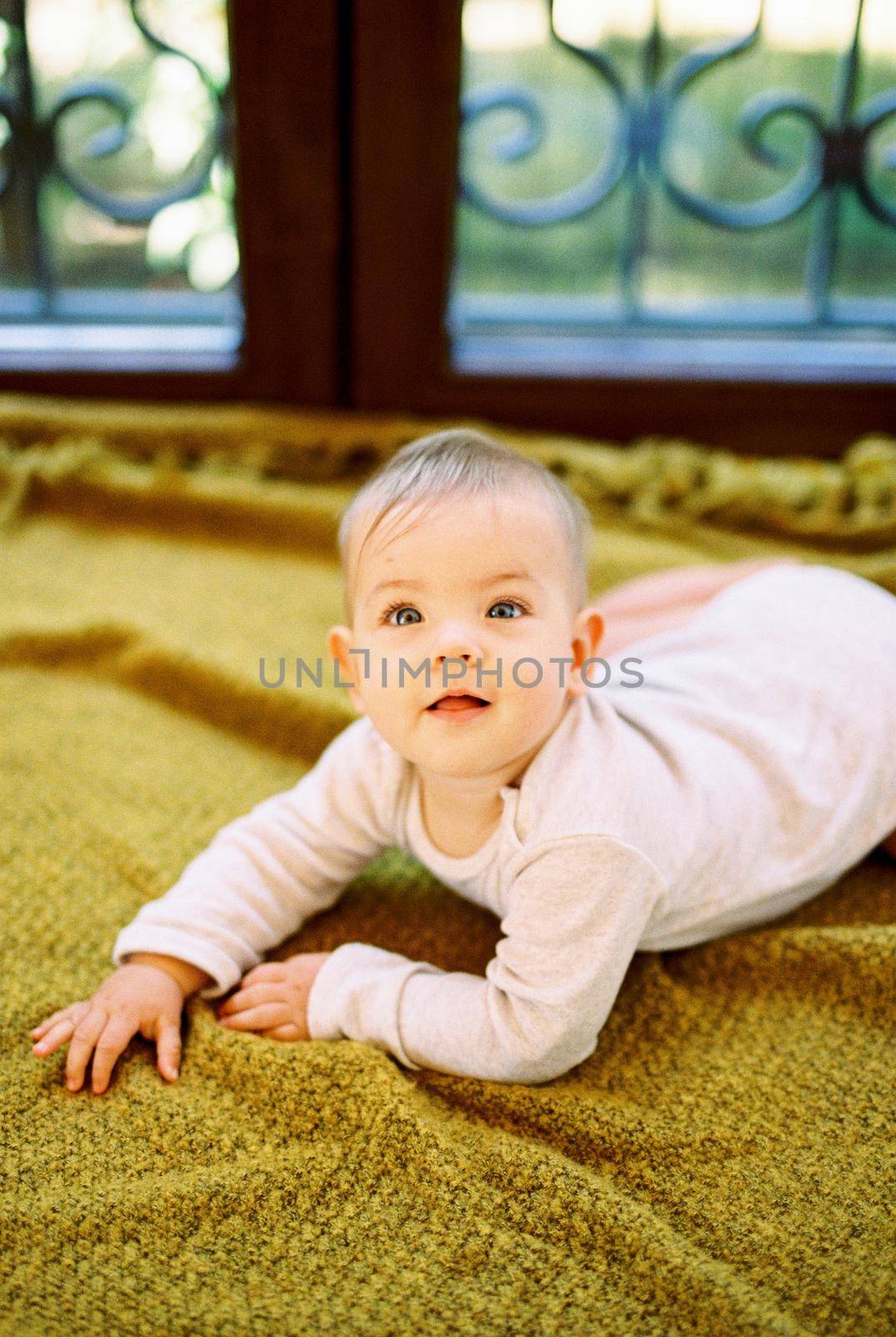 Baby lies on his tummy on a blanket on the floor by Nadtochiy