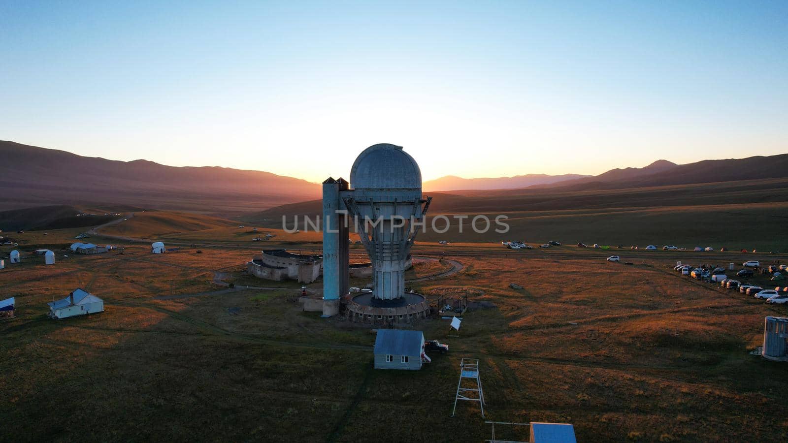 Bright dawn over the Assy-Turgen Observatory in the mountains. Aerial view from the drone of the camp of tents, cars and waking tourists. There is an old abandoned building. Kazakhstan, Almaty