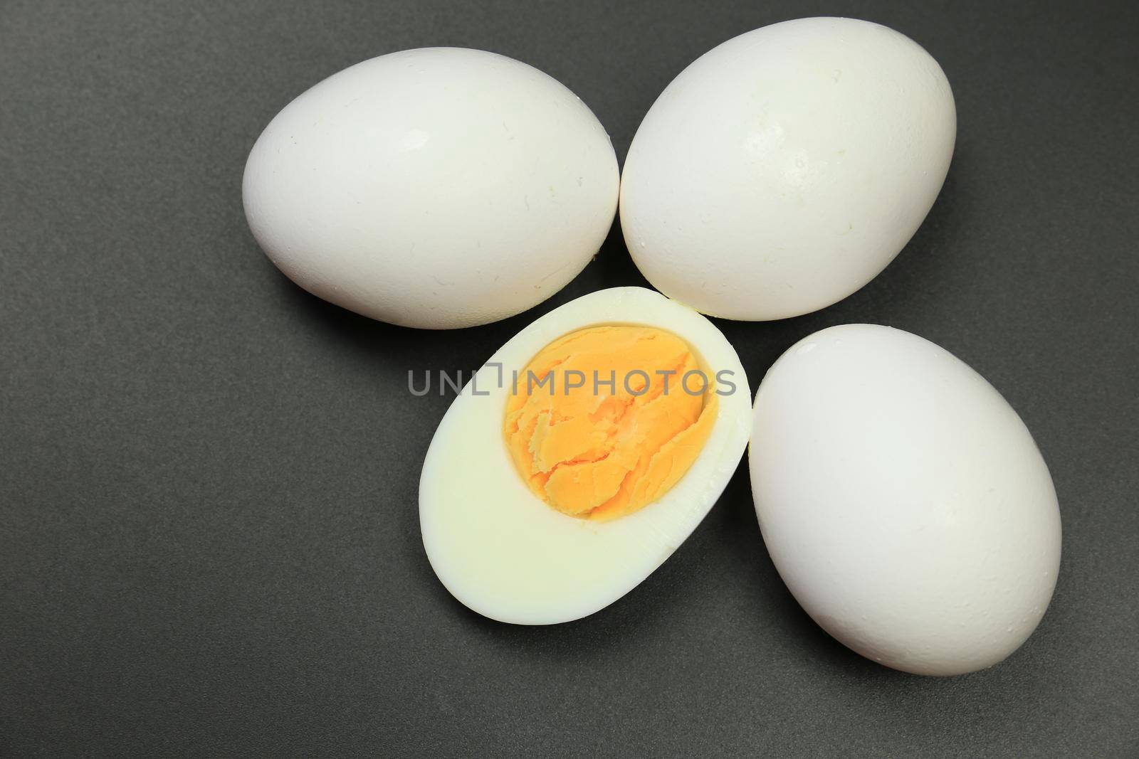 White eggs, one of them boiled and broken in a half on black background