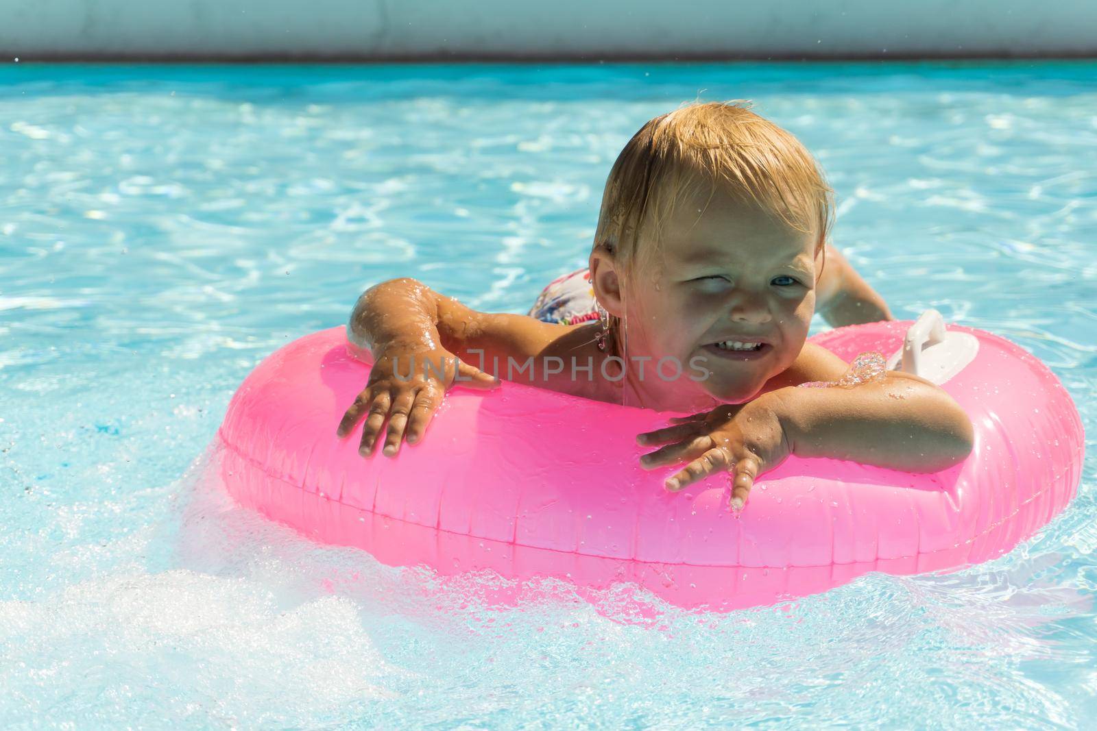 A small child swims in a pink swimming circle in the pool close up