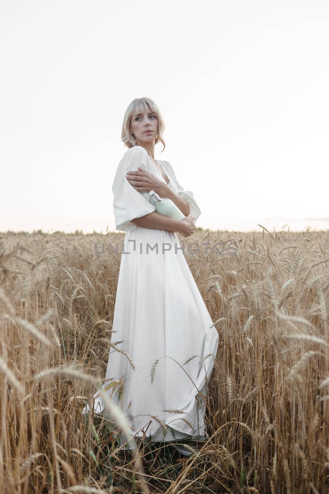 A blonde woman in a long white dress walks in a wheat field. The concept of a wedding and walking in nature by Annu1tochka