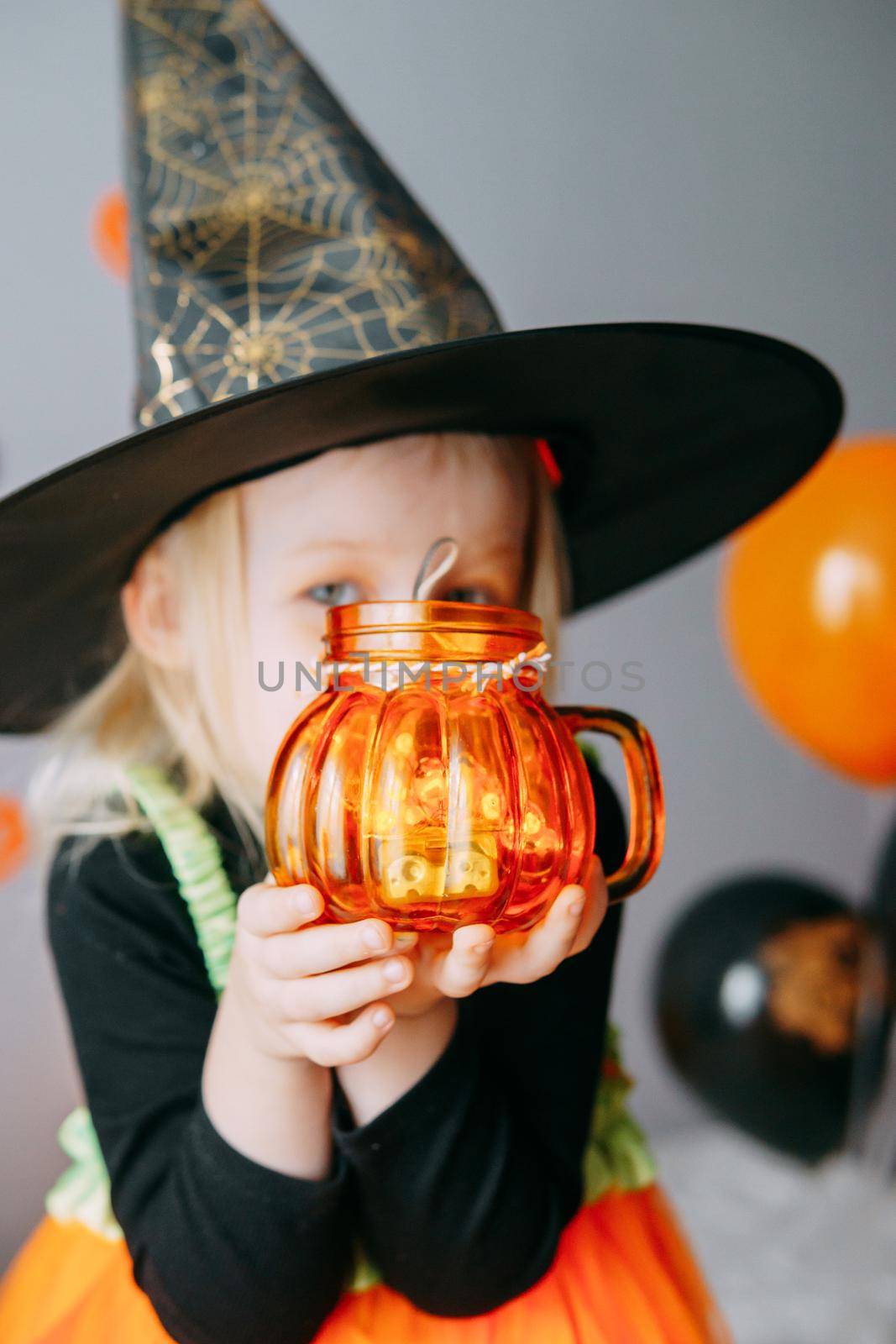 Children's Halloween - a girl in a witch hat and a carnival costume with airy orange and black balloons at home. Ready to celebrate Halloween by Annu1tochka