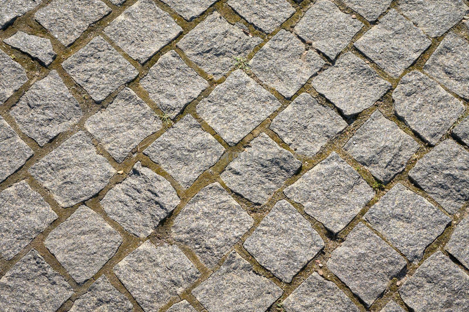 Chipped stone pavement background texture, cobbled street in sunlight.