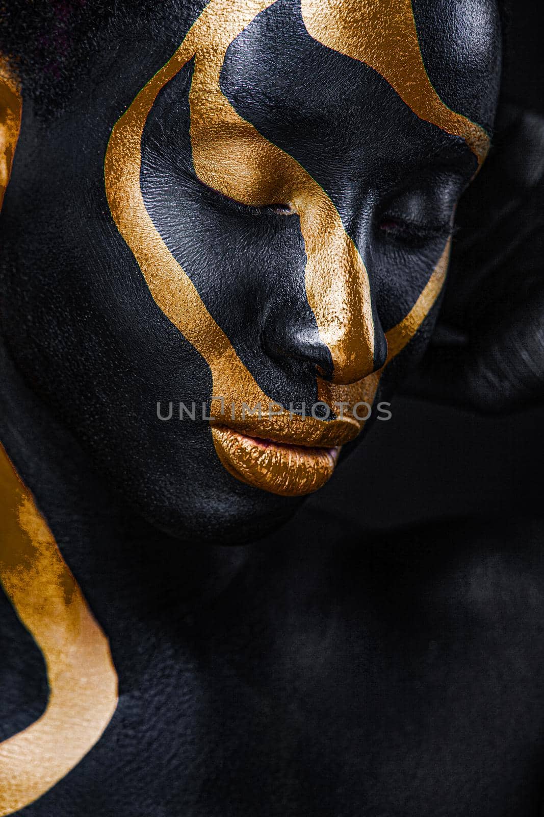 Woman with black and gold body paint. Cheerful young african girl with art bodypaint. An amazing model with yellow makeup. Closeup face. by MikeOrlov