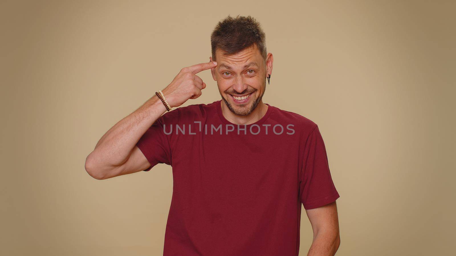 You are crazy, out of mind. Bearded handsome young man pointing at camera and showing stupid gesture, blaming some idiot for insane plan. Adult stylish guy isolated on beige studio background indoors