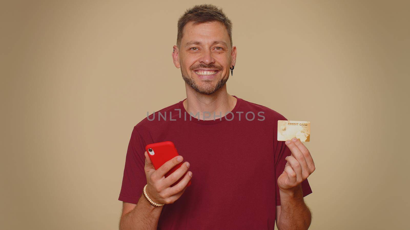 Happy young man use smartphone, plastic credit bank card, browsing say wow yes, found out great big win, success lotter, good news, purchases online shopping. Adult guy on beige studio background