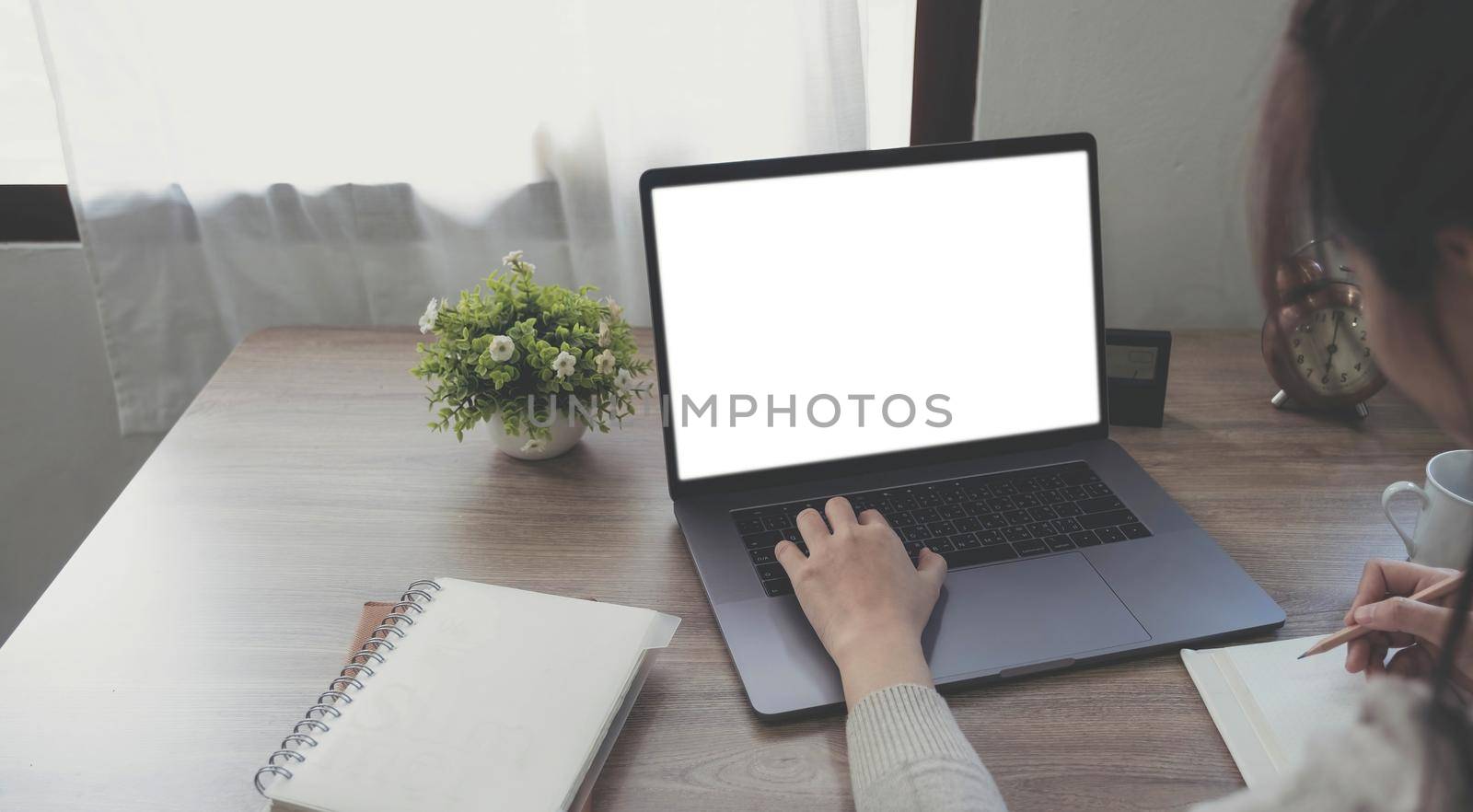 Mockup image of a woman using and typing on laptop with blank white desktop screen on wooden table.