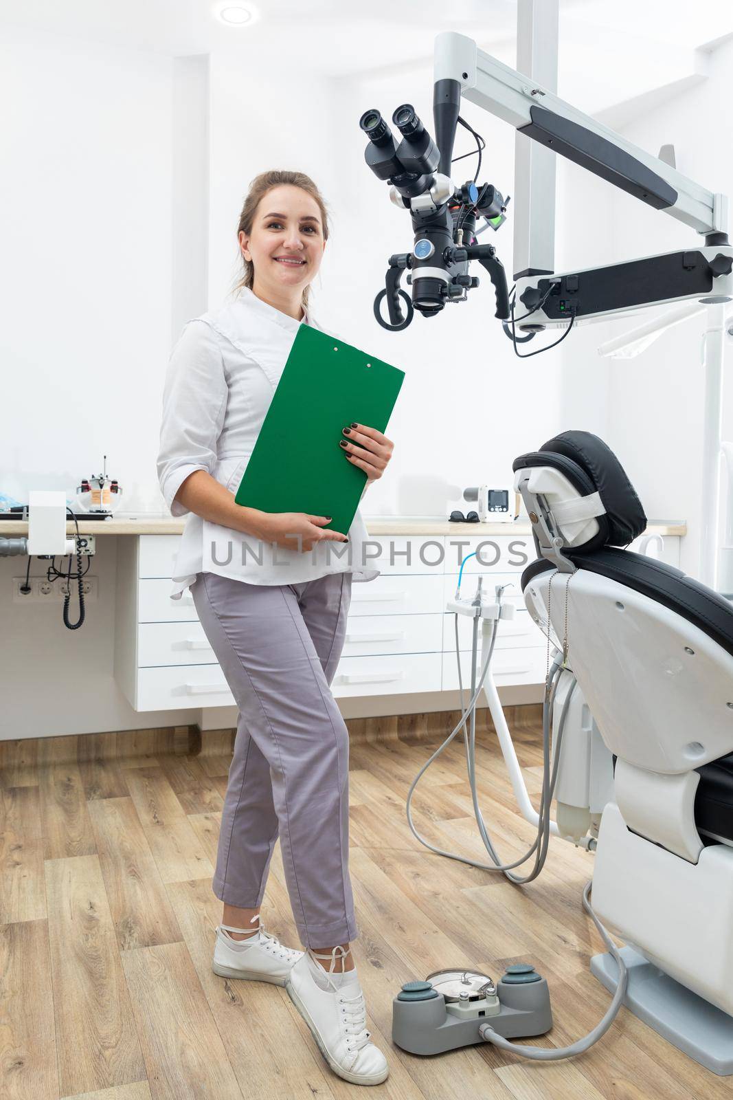 Smiling female dentist holding a clipboard with patient records in hands at dental clinic