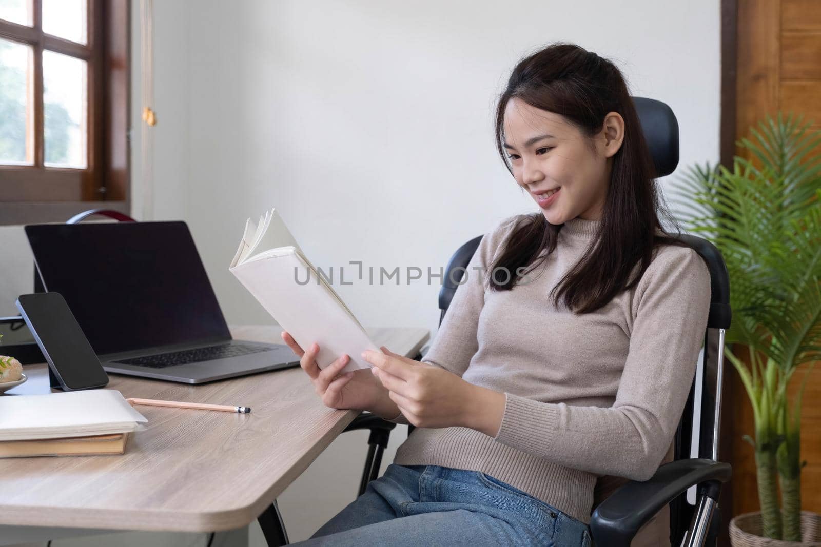 Smiling Asian woman reading book while sitting at home.