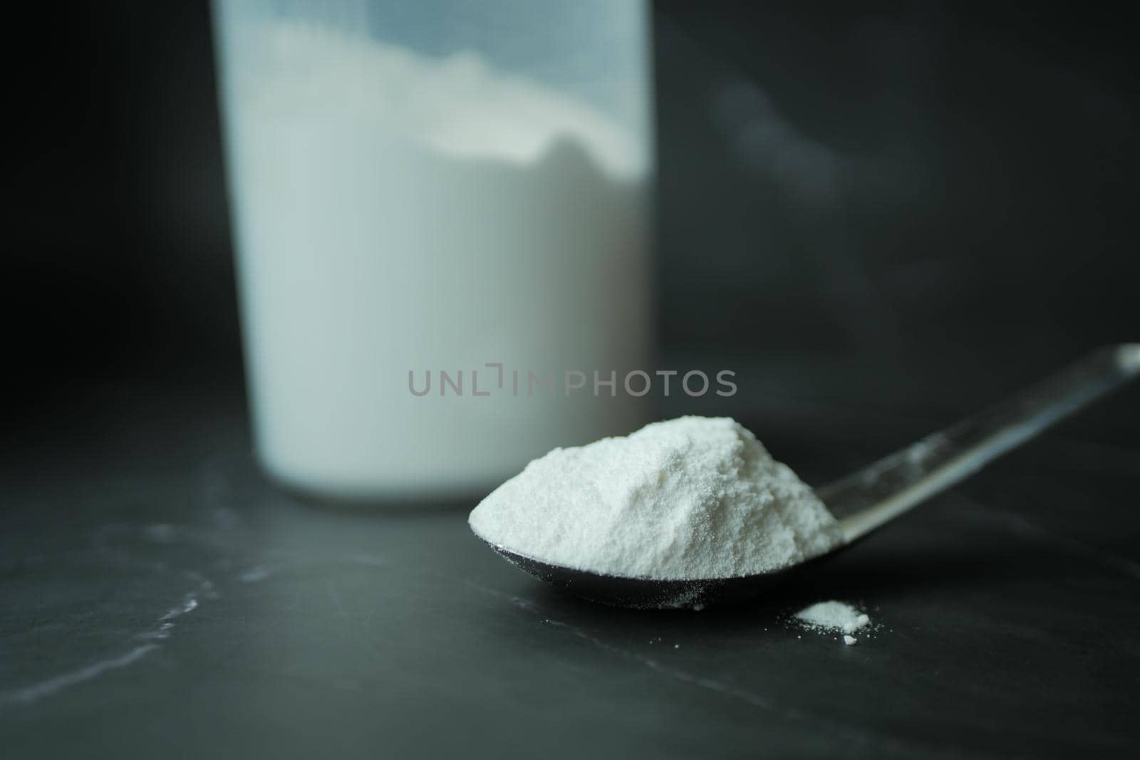 Washing powder in plastic spoon on black background .