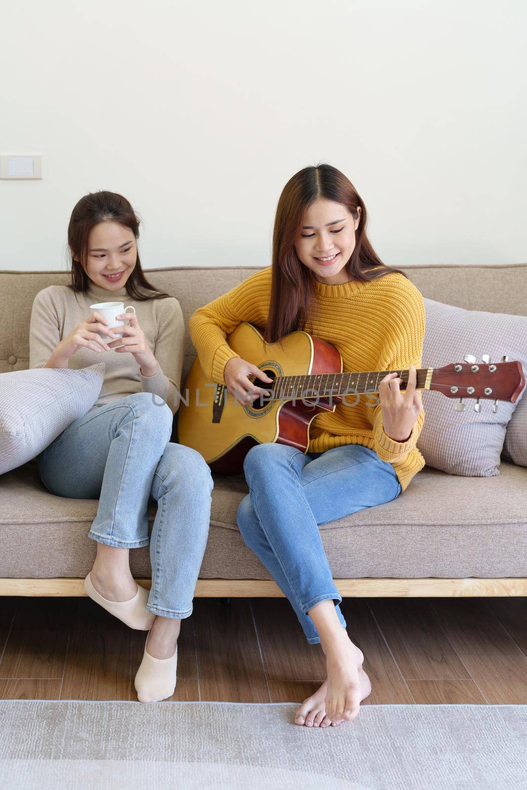 LGBTQ, female couple playing guitar happily on the sofa in the house. by Manastrong