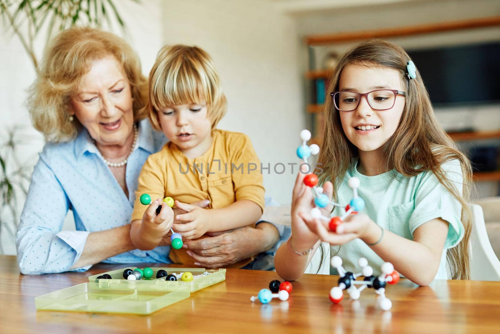 Portrait of grandmother and grandson and granddaughter having fun with a chemistry molecular atom model tool learning biology and chemistry class together at home