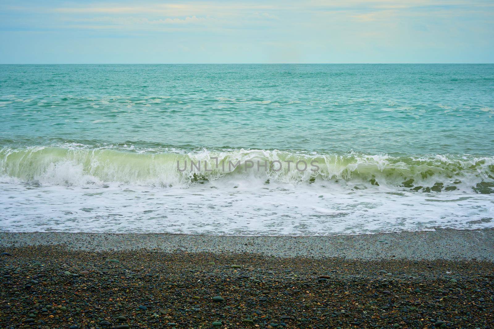 Sea shore with pebbles, wet sea pebbles on the beach and quiet sea surf. Restless sea and waves.