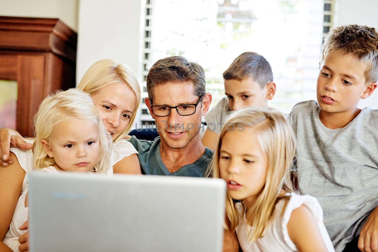 Technology keeps them all entertained. a family using a laptop together at home. by YuriArcurs