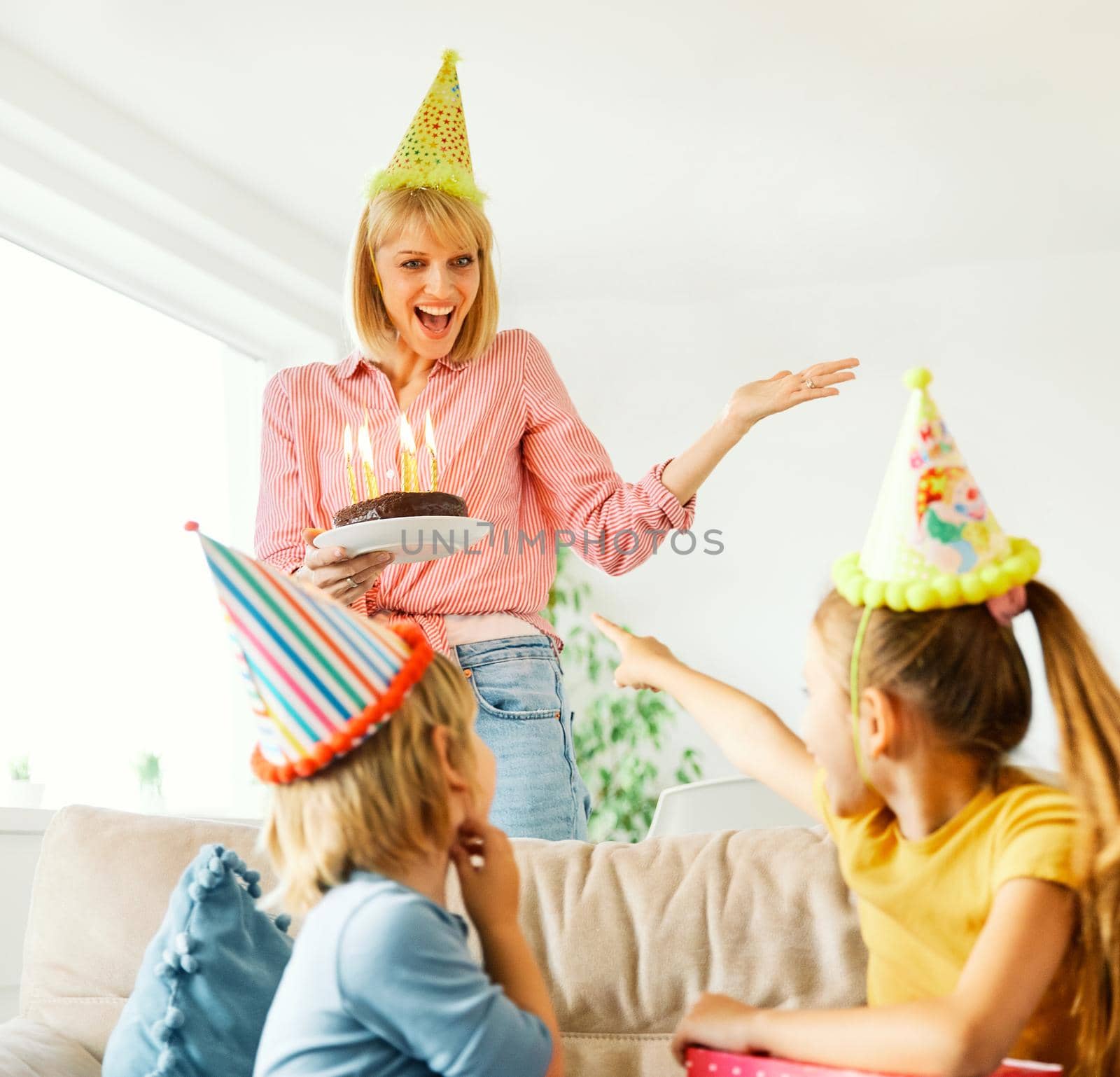 Family of four, mother, father, daughter and son having fun celebrating a birthday together with birthday cake and candles and a present at home