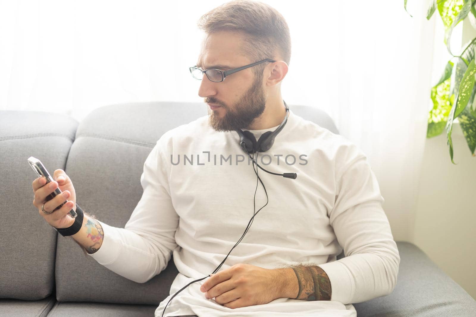 Glad fashionable young bearded guy wears stylish clothes and denim shirt, has trendy hairstyle, happy to exchange messages with friends, uses free internet connection on electronic modern gadget. by Andelov13