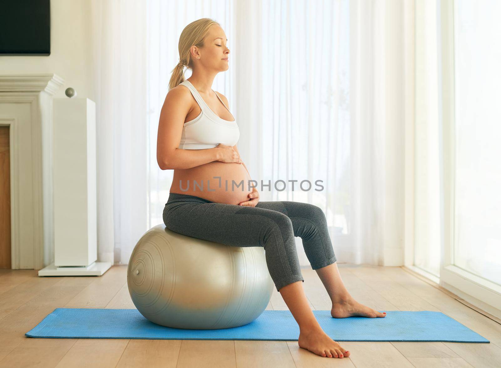 Staying healthy for a stress free pregnancy. a pregnant woman working out with an exercise ball at home. by YuriArcurs