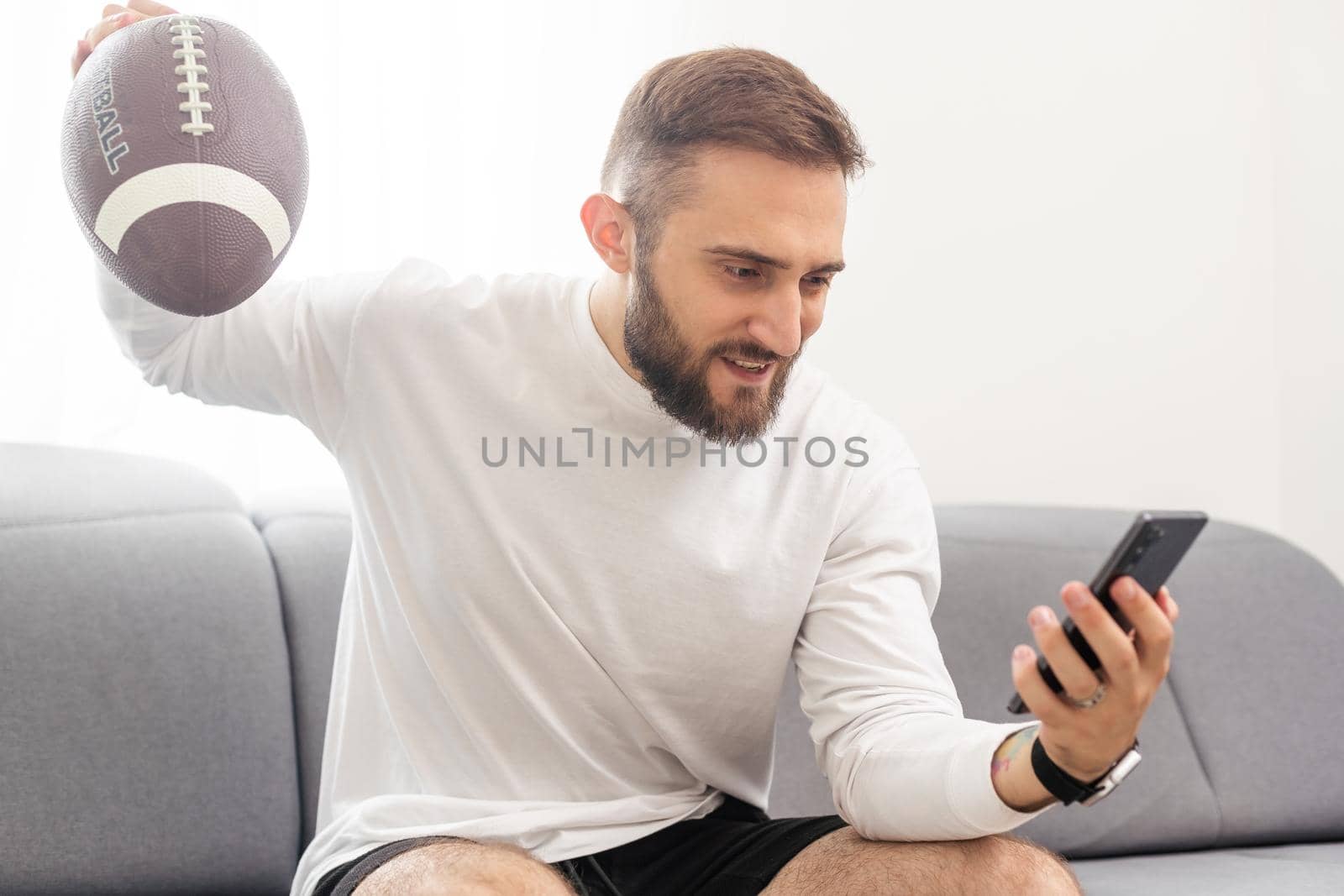 American football fan holding rugby ball and watching match on smartphone by Andelov13