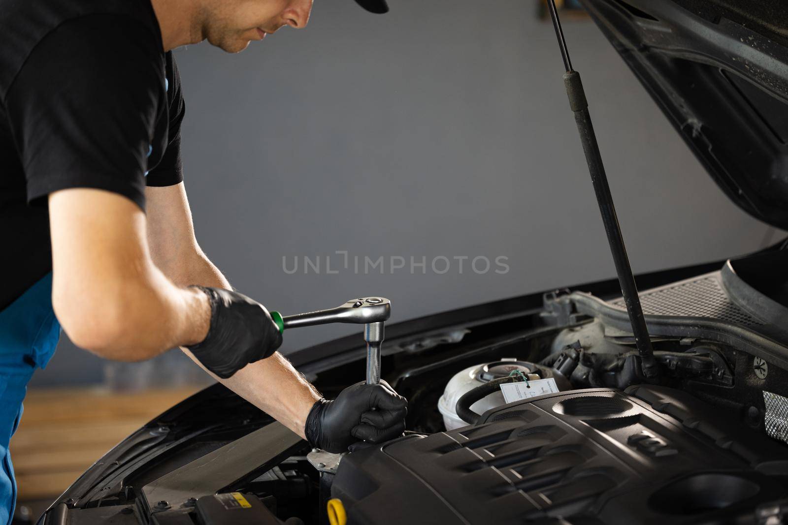 Close Up of male mechanic working on car in a Car Service. Empowering man makes an usual car maintenance. He's using a ratchet. Modern clean workshop. Auto service.