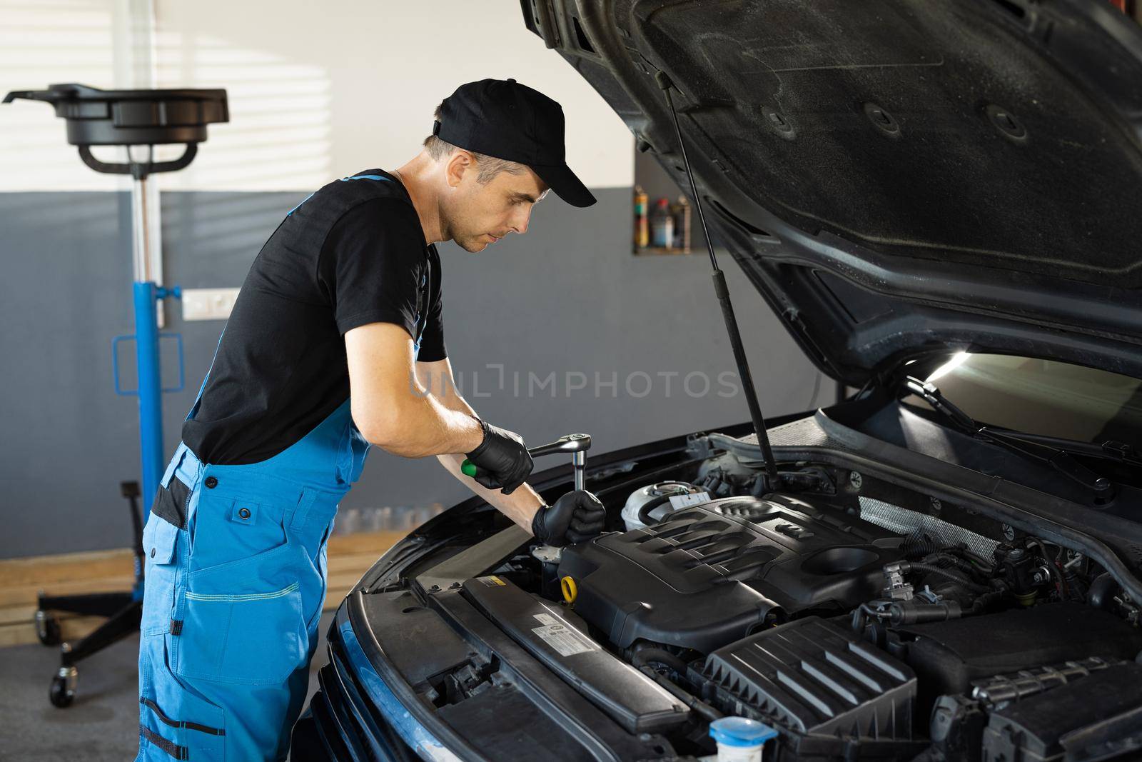 Empowering male mechanic is working in car service. Man is working on an usual car maintenance. He's using ratchet. Car mechanic using wrench to repair the engine, car service. Auto service.