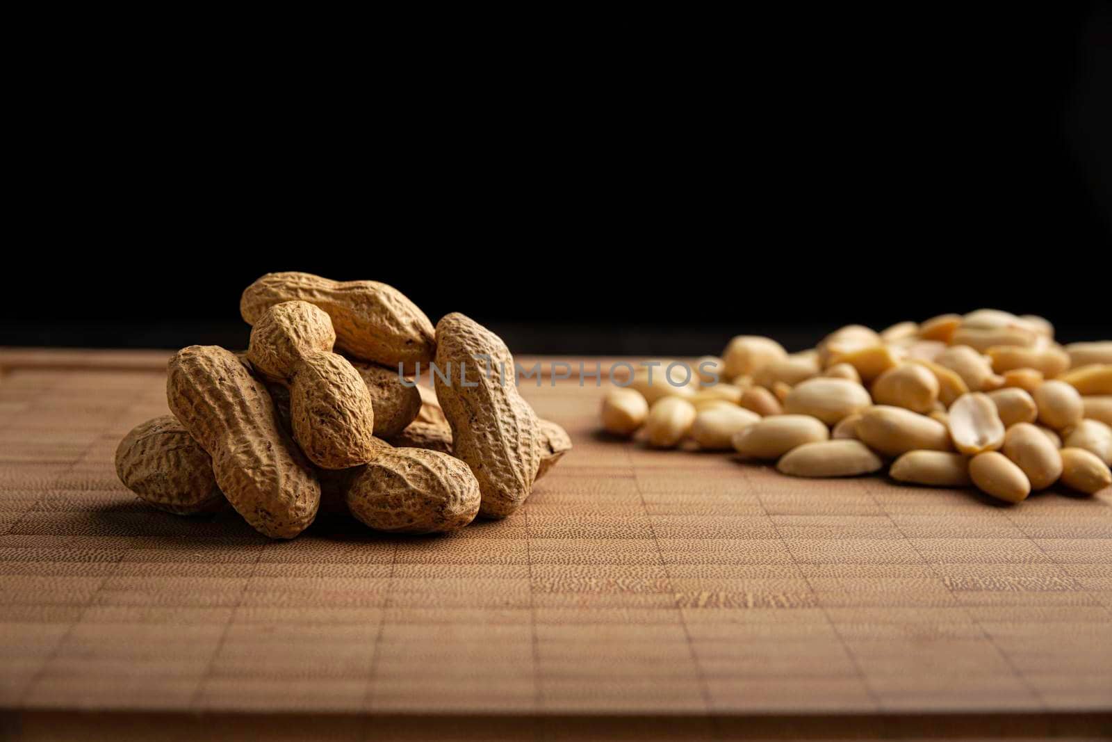 peeled and unpeeled peanuts seeds and on bamboo cutting table with black background. (arachis hypogaea) Edible seeds. Healthy snack nutrition concept