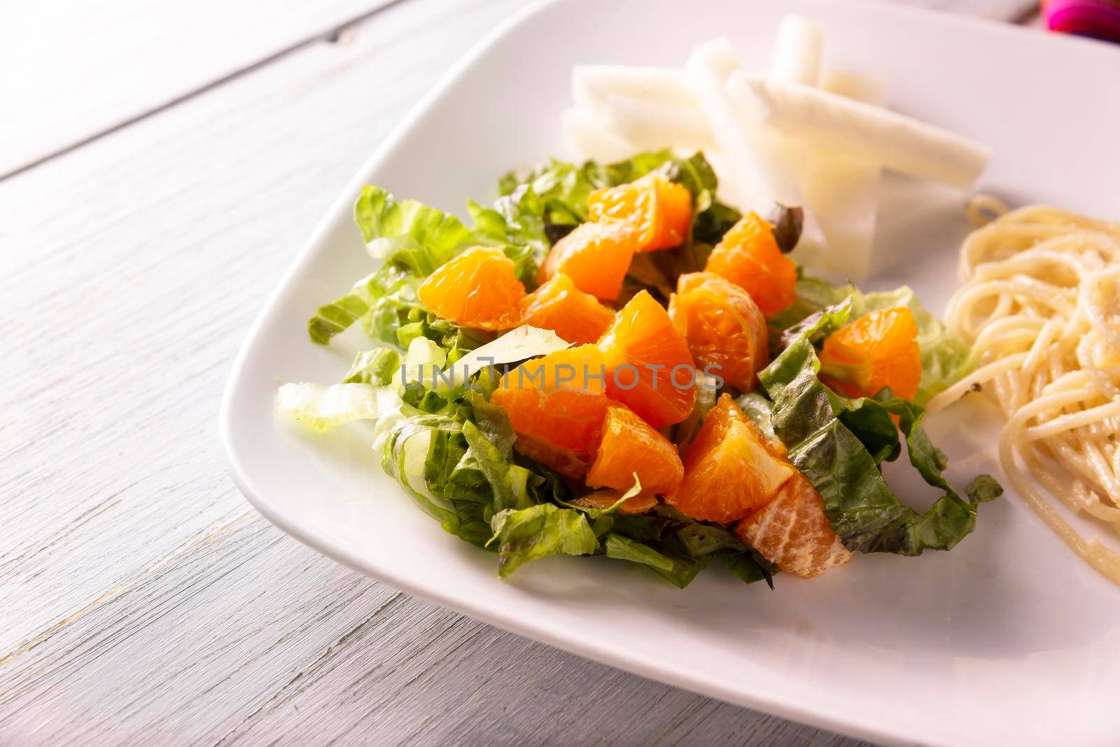 Fresh mixed lettuce and tangerine salad, accompanied by jicama "Pachyrhizus erosus" also known as Mexican yam bean or Mexican turnip. Closeup image.