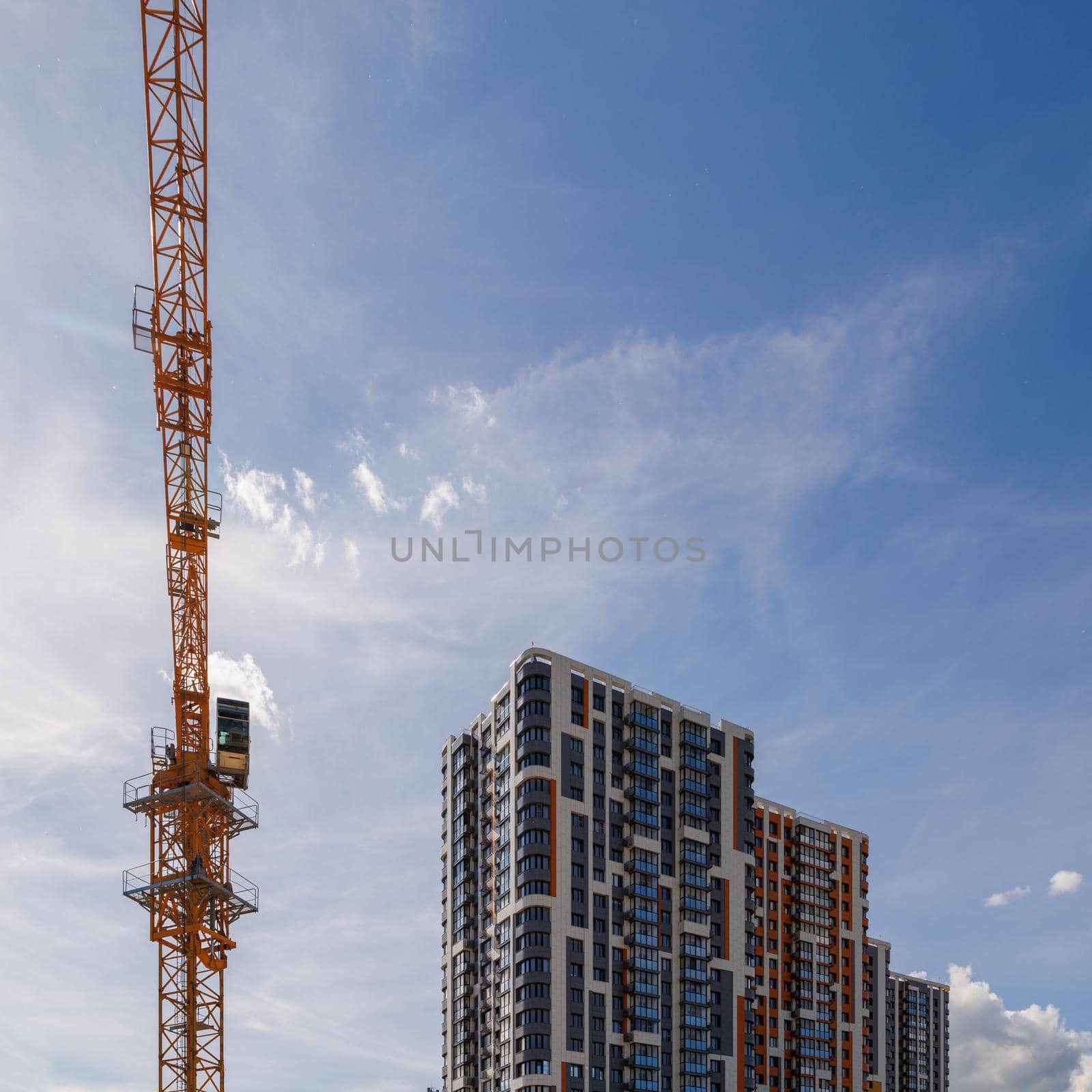 freshly built high rise apartment building near yellow crane on blue sky background with thin feathery clouds.