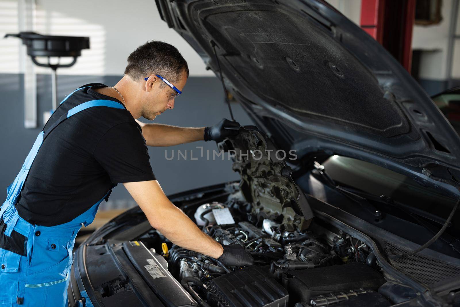 Car mechanic noting repair parts during open car hood engine repair at garage. Mechanic man open a car hood and check up the engine. Overheating of a car engine. Motor with open hood by uflypro