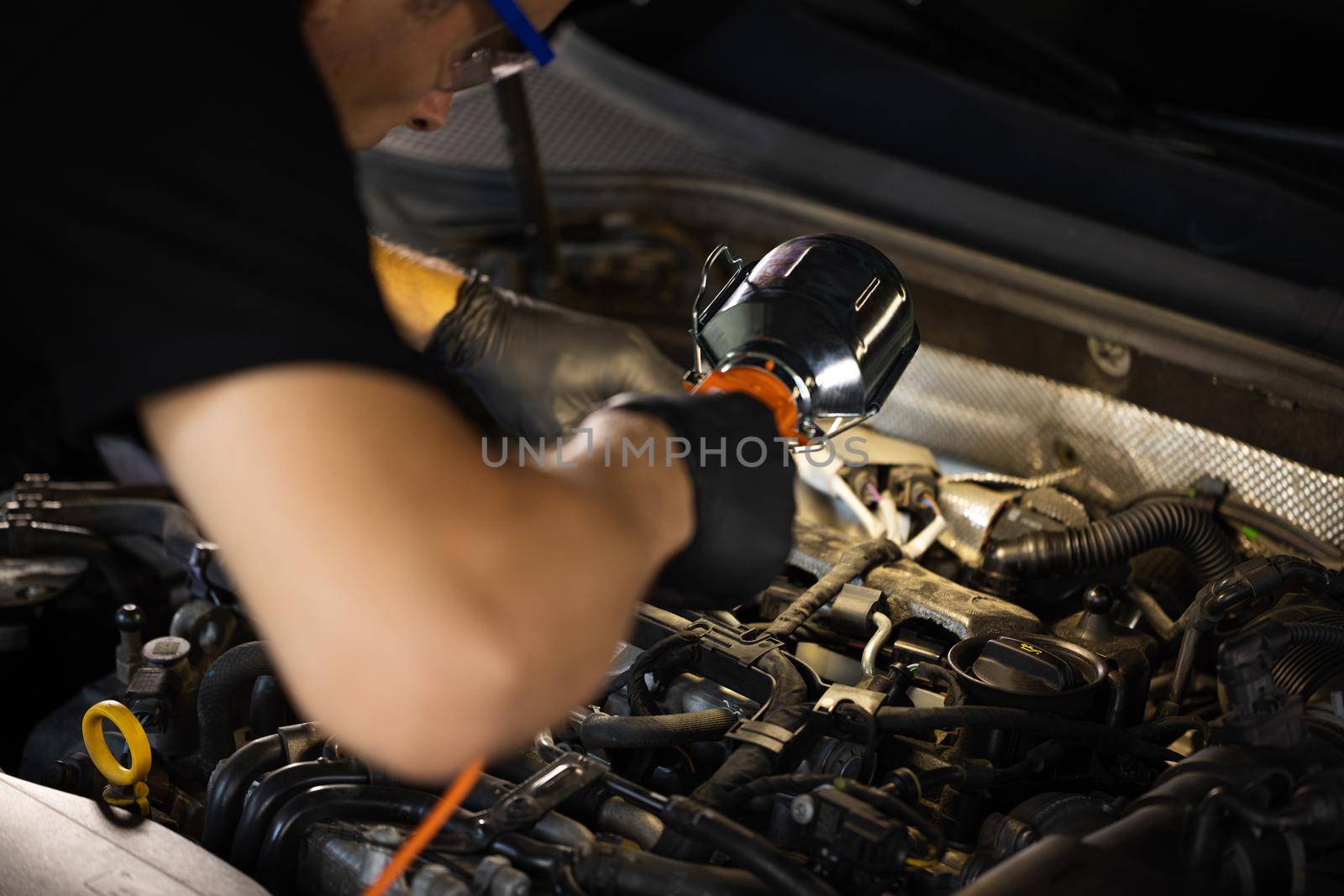 Repairman in Safety Glasses is Working on an Usual Car Maintenance. Mechanic is Working on a Car in a Car Service. He Hangs Led Lamp. Modern Workshop by uflypro