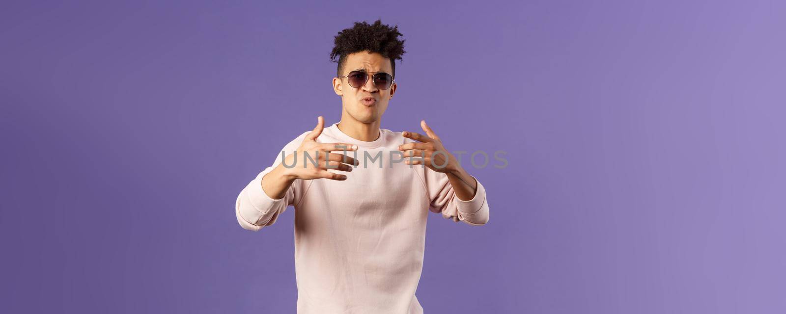 Portrait of sassy and carefree young hipster guy with dreads, wearing sunglasses dancing and gesturing while singing during rap battle, dance hip-hop on party, standing purple background by Benzoix