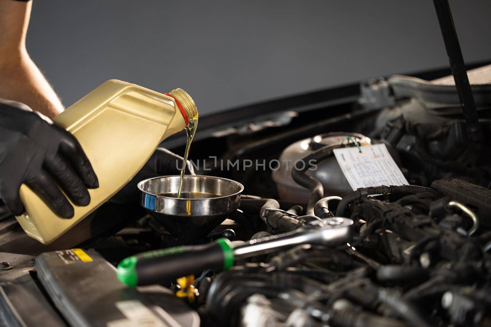 Pouring Oil from Plastic Container. The mechanic is pouring oil into the engine by uflypro
