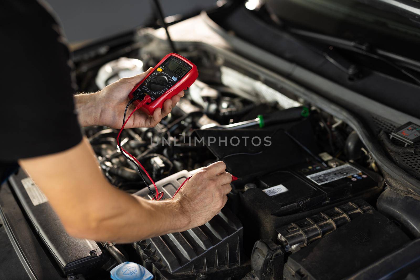 Automobile diagnosis. Car mechanic repairer looks for engine failure on diagnostics equipment in vehicle service workshop. Professional car mechanic check battery voltage with electric multimeter.