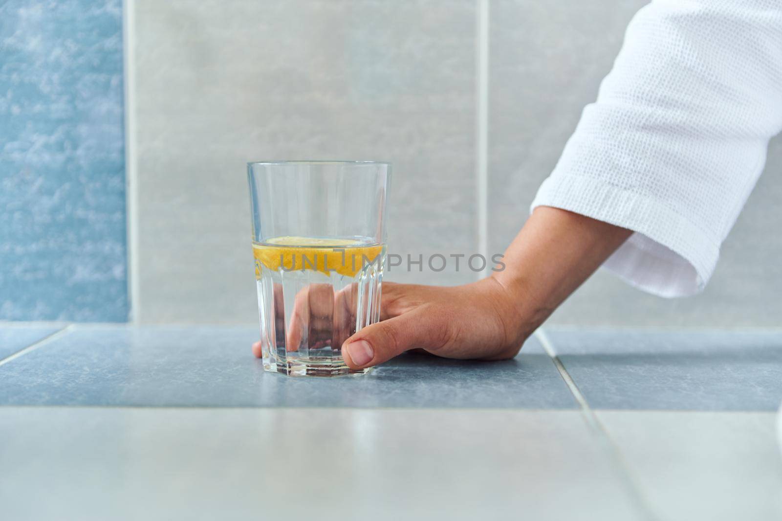 Close-up. Details: woman hand holding a drinking glass with fresh antioxidant lemon water. Morning drink for weight loss. Dieting. Healthy habits. Morning routine for good start to the day. Body care