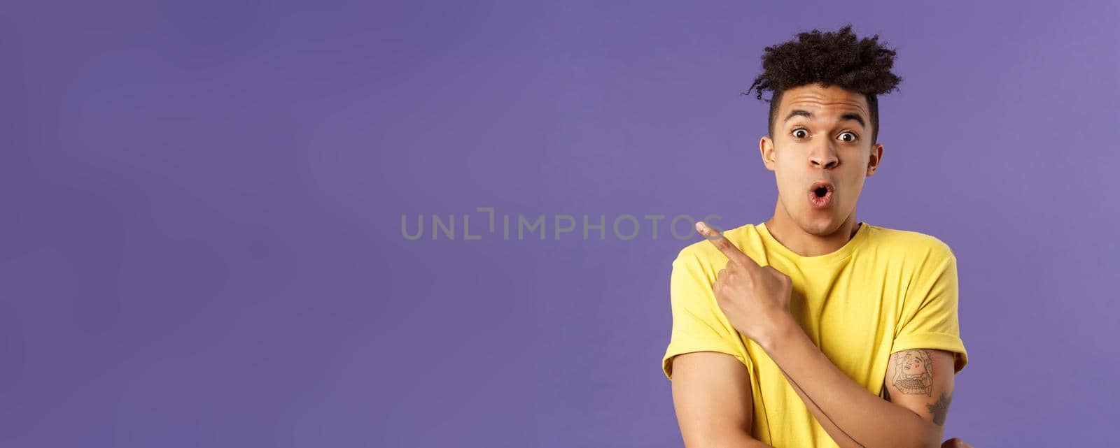 Portrait of surprised, excited young man showing cool new thing, pointing upper left corner, gasping, folding lips, stare camera impressed say wow, standing purple background by Benzoix
