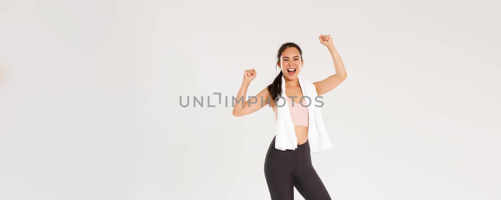 Sport, gym and healthy body concept. Full length of happy asian brunette girl, slim female athelte in active wear, shouting yes and raising hands up motivated to workout, enjoy training in gym by Benzoix