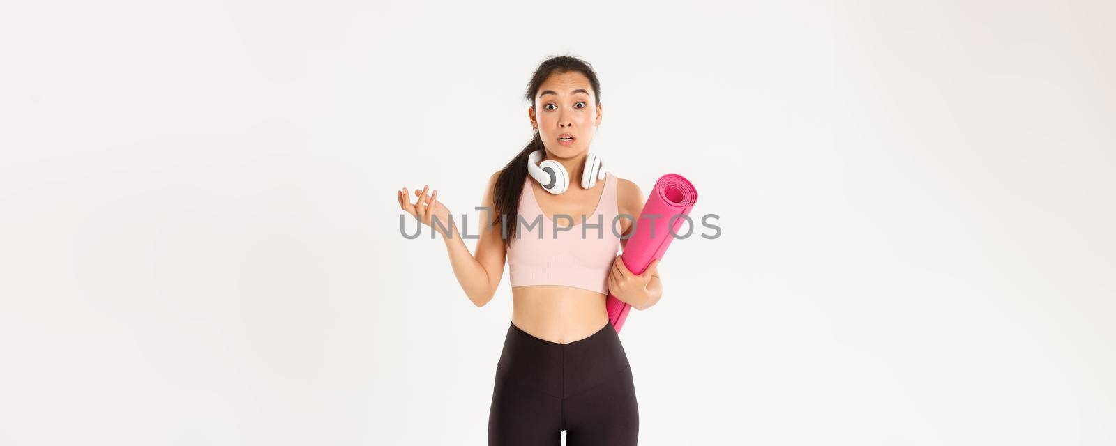 Sport, wellbeing and active lifestyle concept. Confused and shocked asian fitness girl, cant understand why gym closed, holding rubber mat and looking surprised at camera, white background by Benzoix