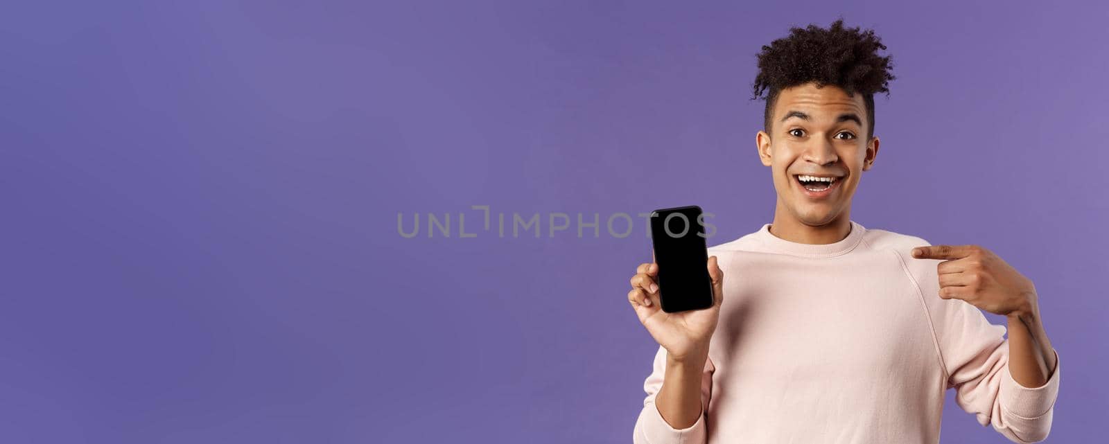 Portrait of excited, happy smiling man talking about new application or game feature, pointing at smartphone display, talking about mobile phone with amused cheerful expression by Benzoix
