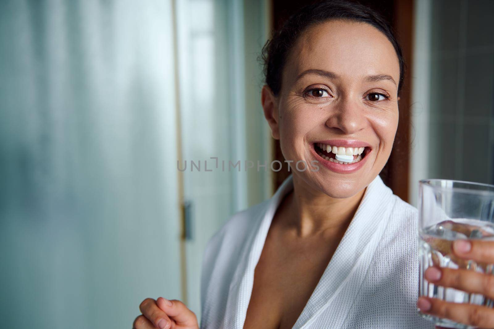 Happy multiethnic woman smiling toothy smile, looks at camera, taking pills for antidepressant therapy, according to doctor's prescription. Mental health concept. Treating depressing and panic attacks