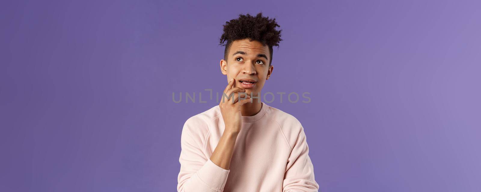 Waist-up portrait of thoughtful unsure young hispanic male student trying solve exercise, looking up thinking, pondering and calculating in mind, standing focused and indecisive purple background.