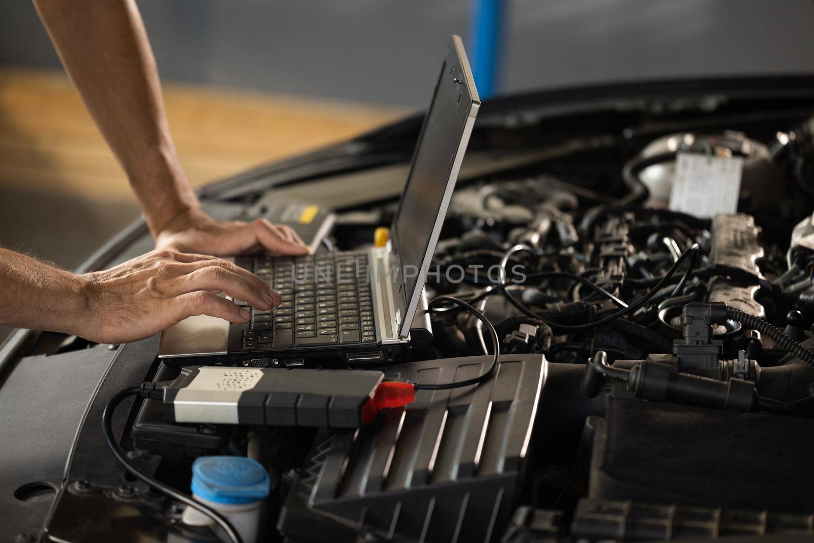 Auto mechanic uses laptop while conducting diagnostics test. Modern car service. Computer diagnostics of the car. European car mechanic holds a digital device.